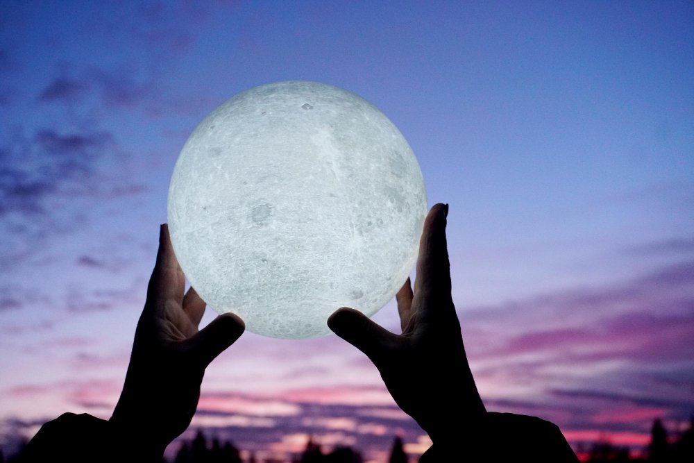 una luna entre las manos de una persona mirando al cielo